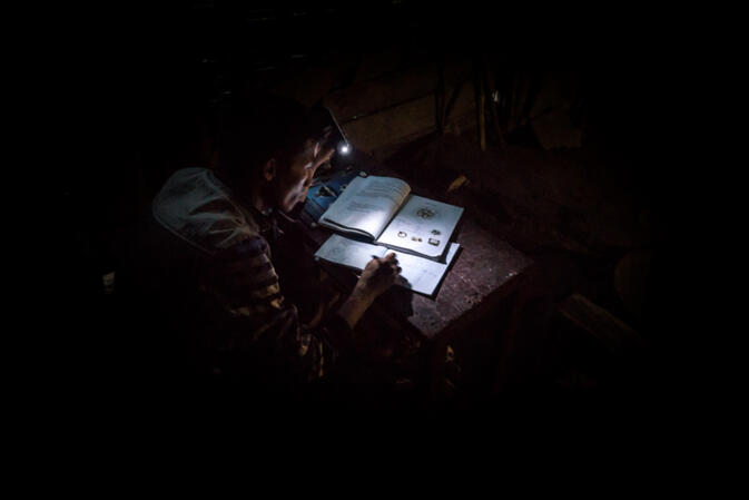 A man does his homework by the light on his cellphone in the remote Hmong village of Ban Sam Soun, Laos. This village has no running water or electricity, yet is located on a paved road next to power lines (photo credit: 	Will Stauffer-Norris)