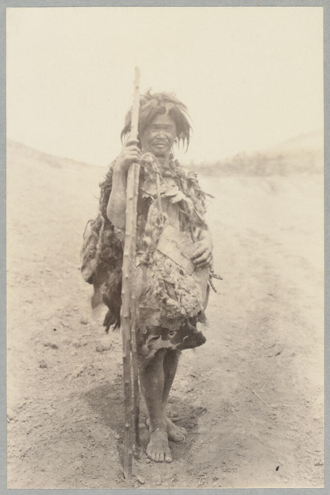 Full body view of man in native dress carrying sticks May 10, 1922